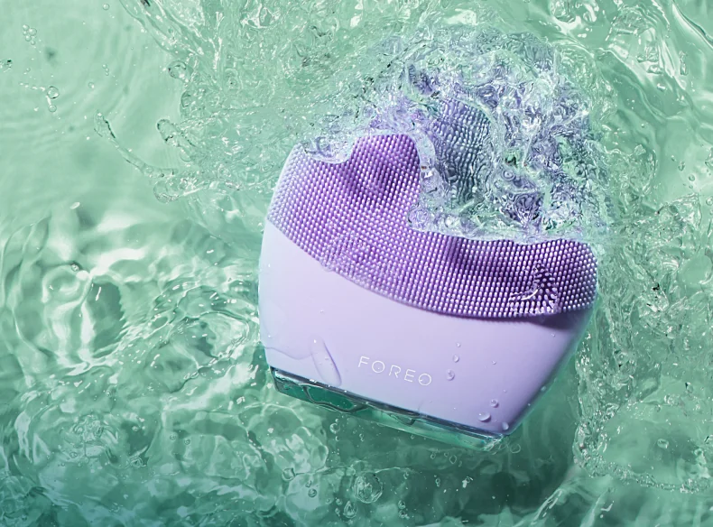 Lavender FOREO LUNA cleansing device resting in clear rippling water
