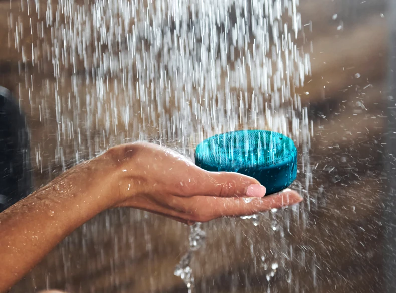 Teal FOREO LUNA 4 body brush held in an open hand under running shower water