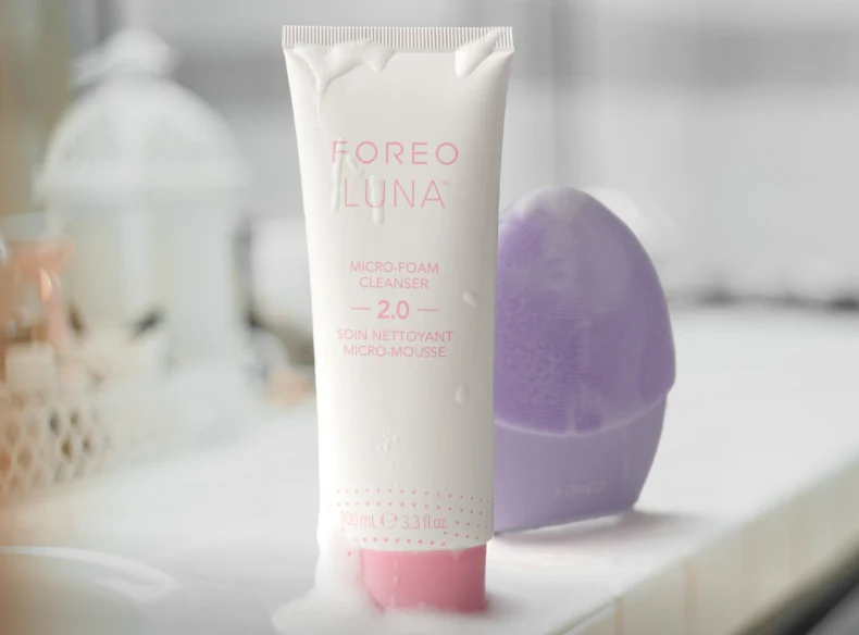 Tube of FOREO LUNA Micro-Foam Cleanser 2.0 beside a lavender LUNA device on a bathroom counter