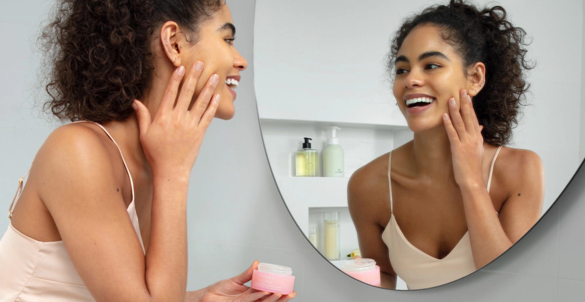 Woman massaging FOREO LUNA Ultra-Nourishing Cleansing Balm onto her face in front of a round mirror