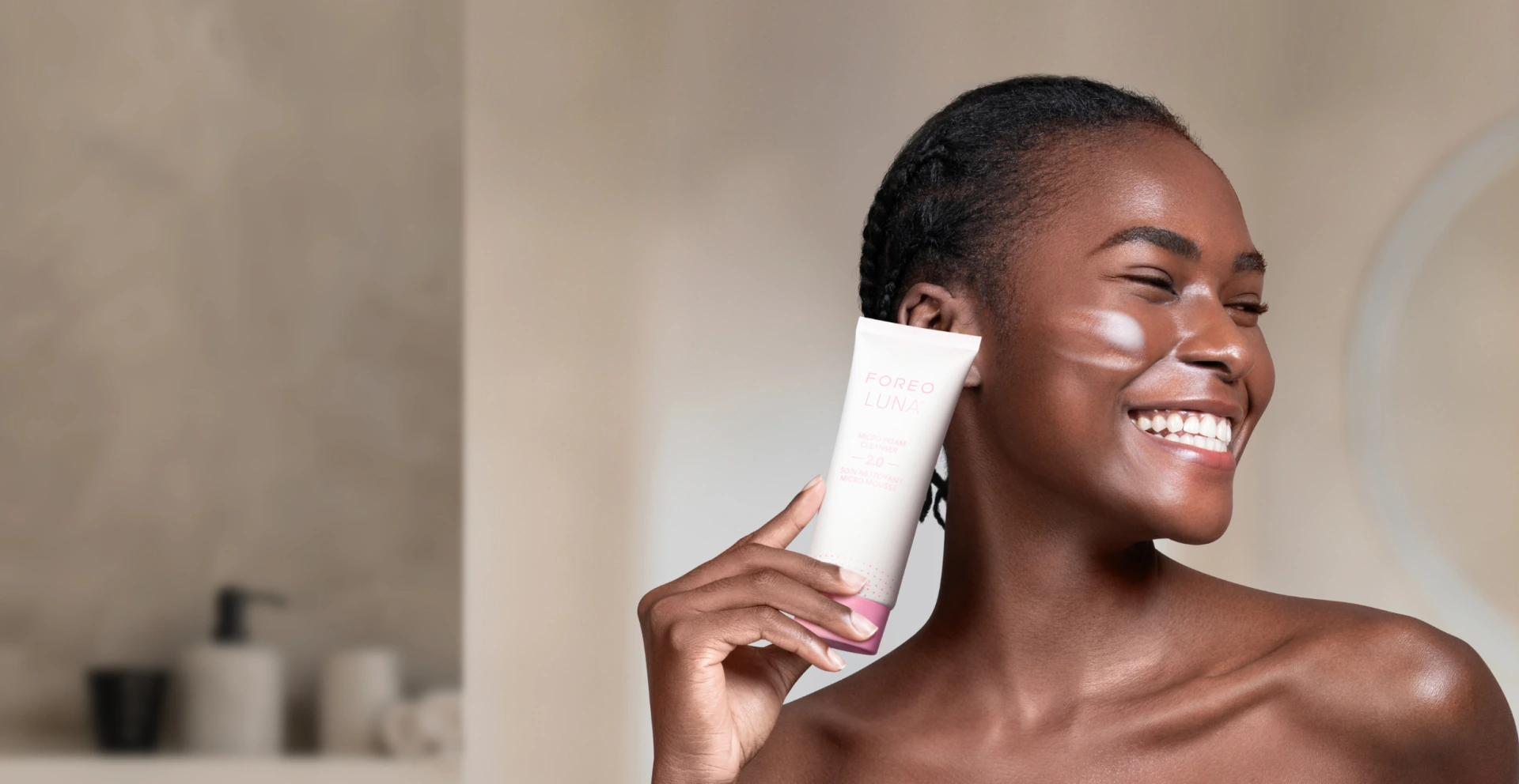 Smiling woman holding a tube of FOREO LUNA Micro-Foam Cleanser 2.0 to her cheek