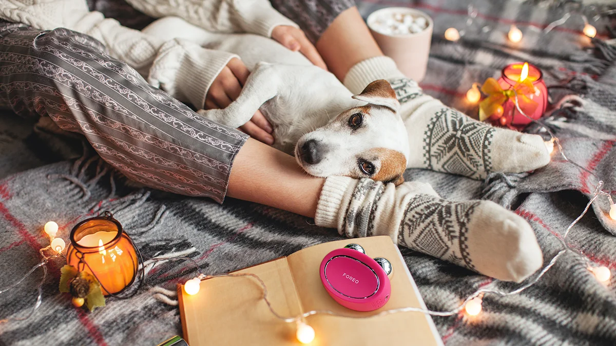 A woman with a BEAR 2 microcurrent therapy device, comfortably relaxing at home with a dog and a book 