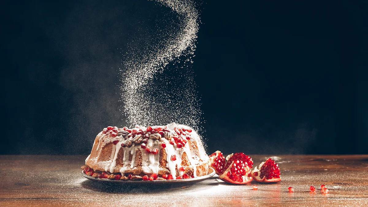 A kuglof cake on dark bacground with icing sugar falling on it in a spiral