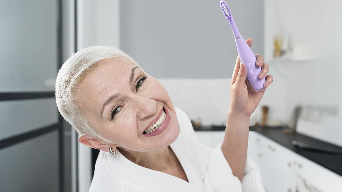 A mature beautiful woman with a buzzcut smiling and using Issa 4 sonic toothbrush for sensitive teeth