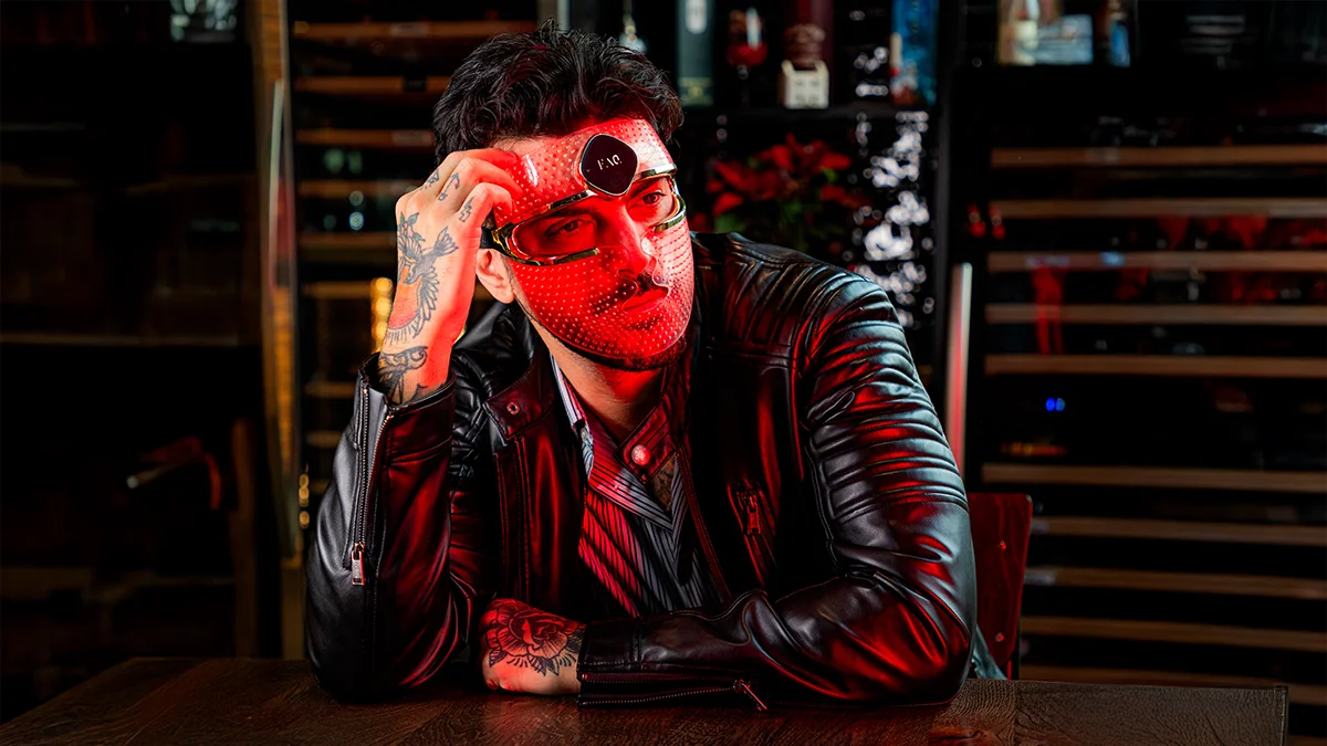 An atractive exotic man with tatoos wearing the FAQ 202 red light face mask