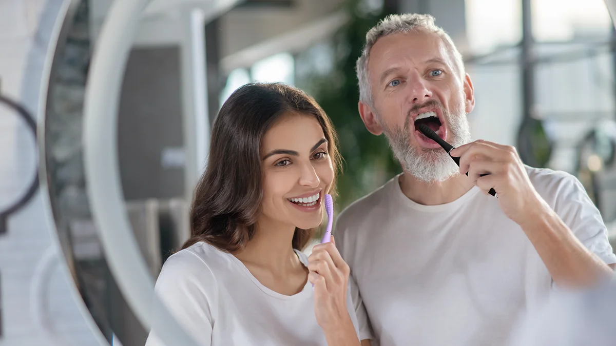 an attractive couple using issa 4 silicone sonic electric toothbrush in front of a mirror at home