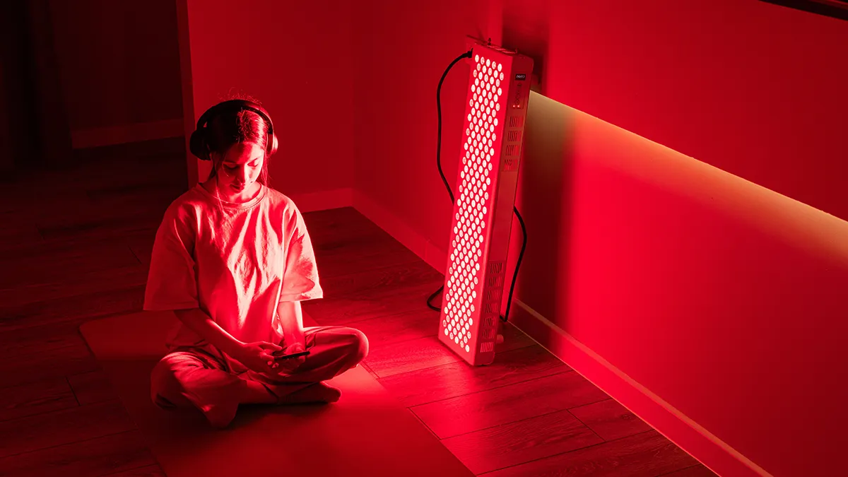 A woman sitting in front of an LED red light therapy panel