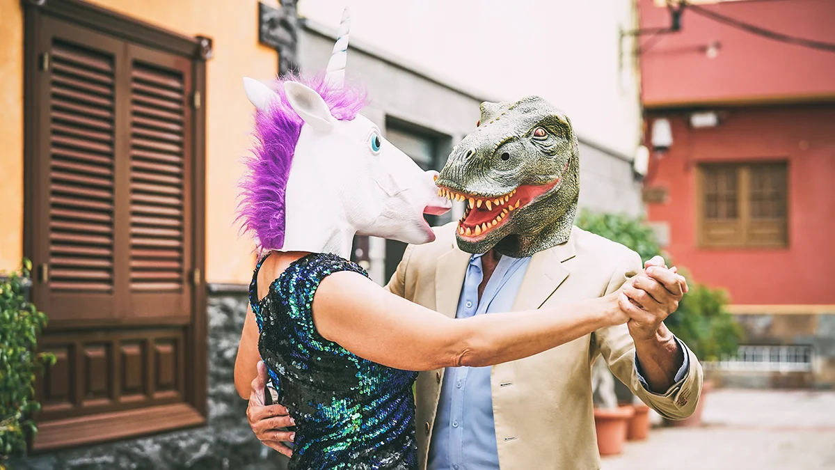 A man and a woman enjoying a romantic dance in the steets wearing a unicorn and a T-rex face masks