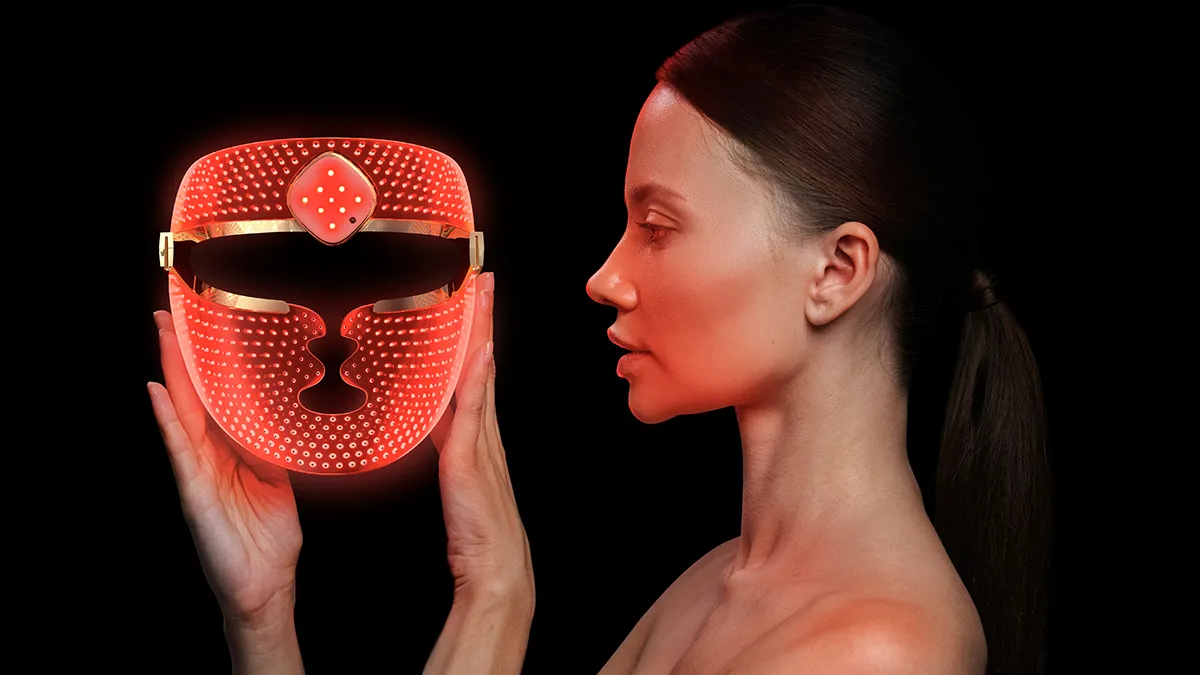 A woman side profile holding a FAQ 202 plus red light therapy mask on black background
