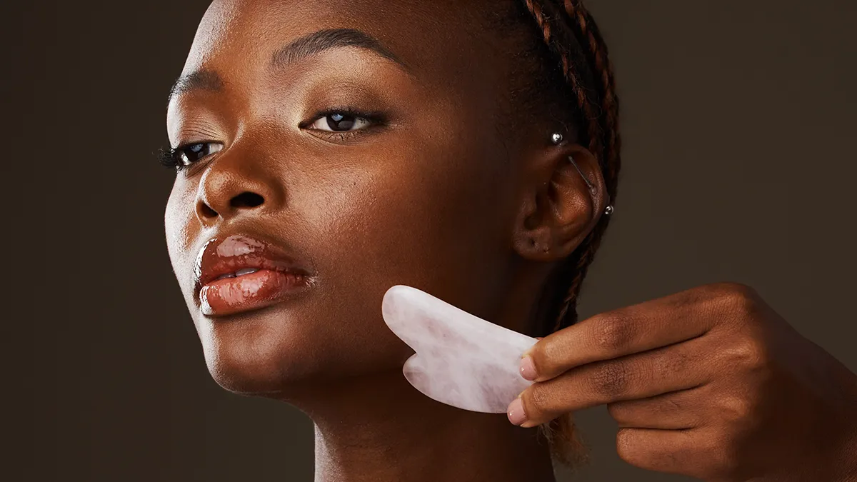 A beautiful African-American woman doing lymphatic drainage massage for face with gua sha