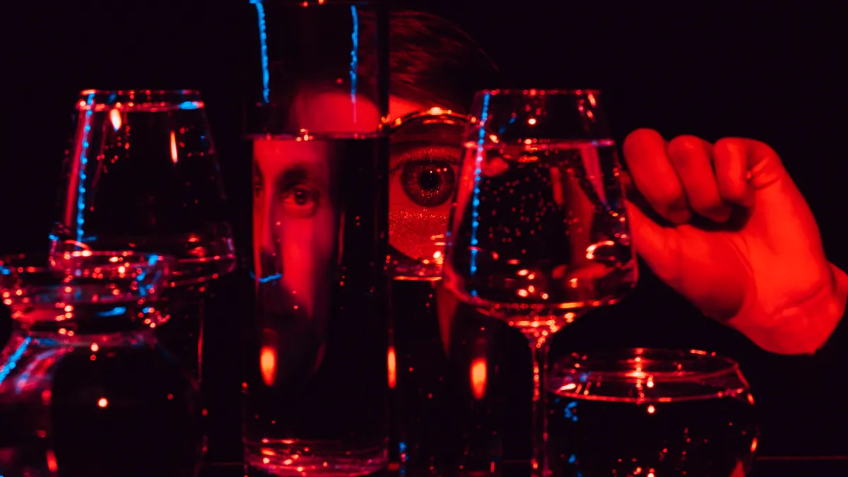 A face in red light distorted behind glasses with water on a dark background