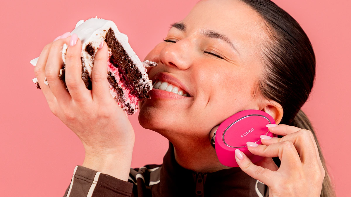 A happy woman eating cake while doing microcurrent facial toning excercises with BEAR 2 microcurrent device