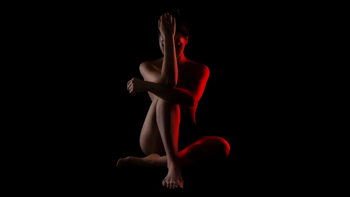 A naked woman in the dark with a red light shining on her