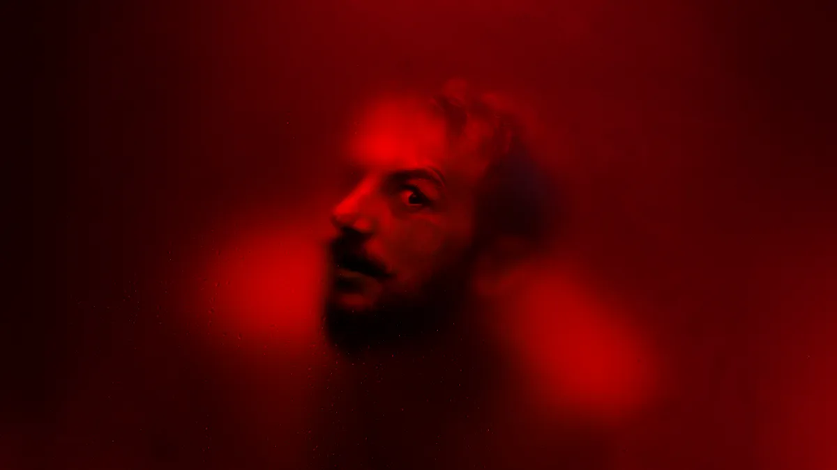 A male head pressed against a red glass, looking straight at you