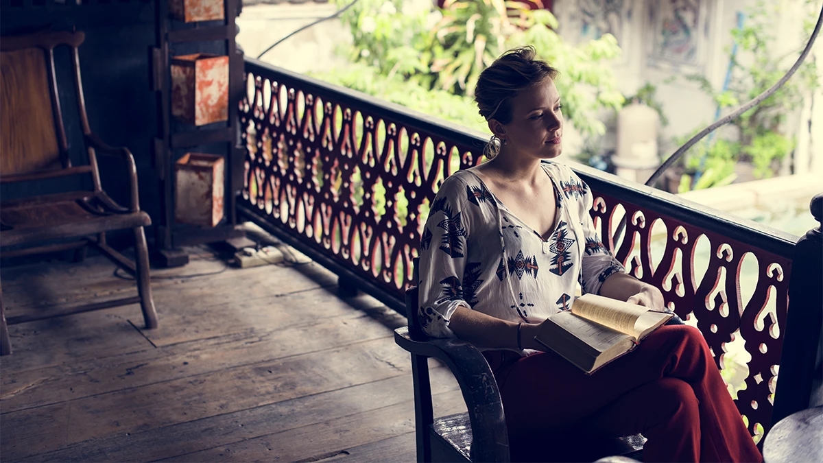A woman reading on a shaded terrace above a beautiful green garden