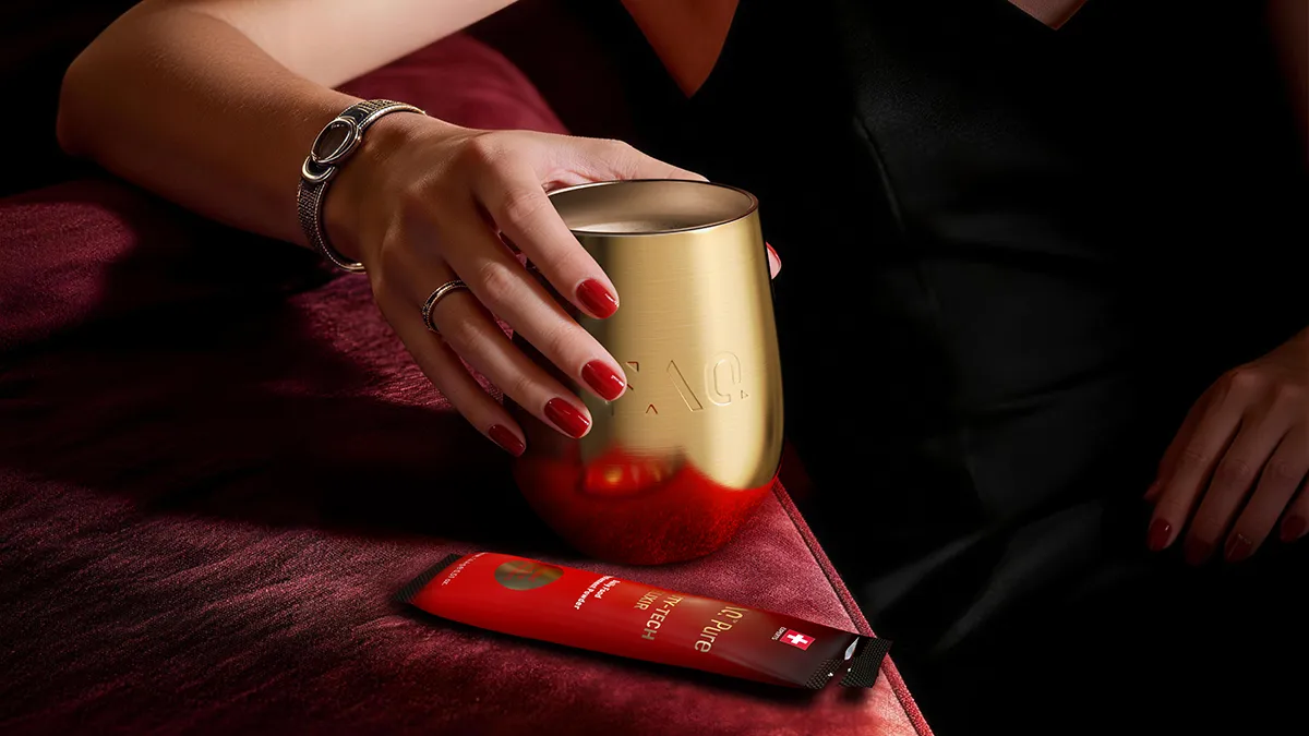 A woman with red nails holding a gold glass of FAQ Pure Beauty Tech Elixir gut health supplement