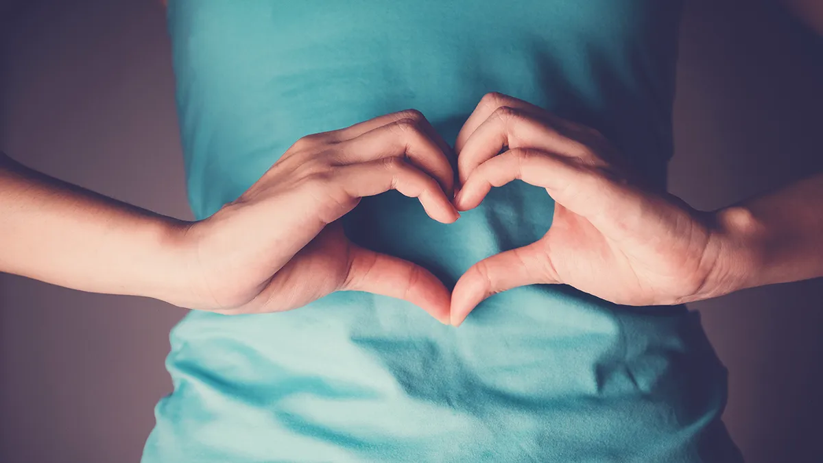 A woman making a sign of heart with her hands in front of her stomack