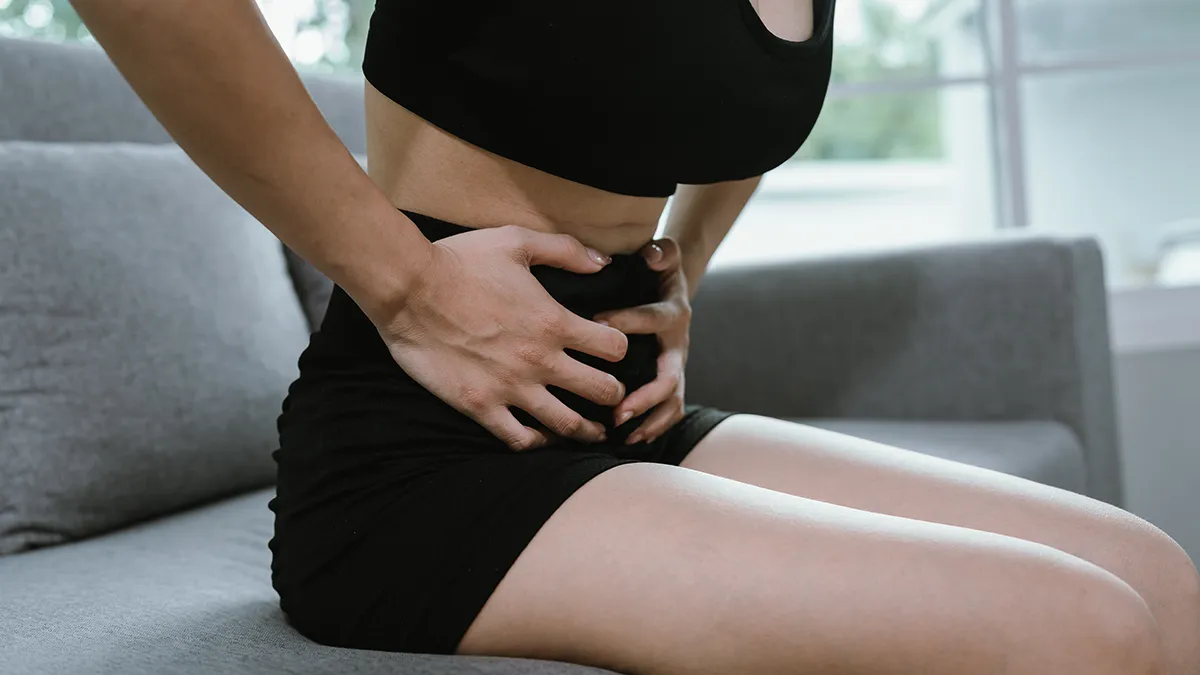 A woman sitting down in black underwear with a pain in her stomack