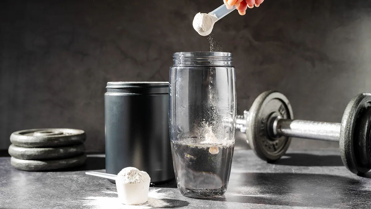 A hand putting some creatine powder into a gym bottle on a dark background
