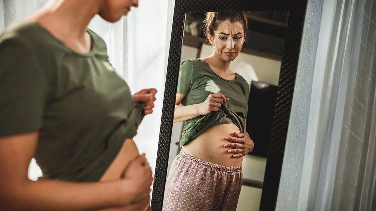A woman looking at her bloated stomack in the mirror