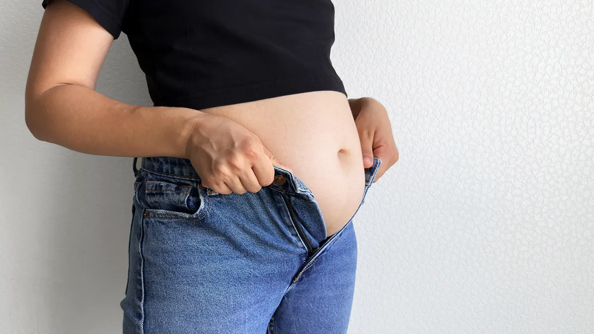 A woman trying to button jeans and wandering how to reduce bloating