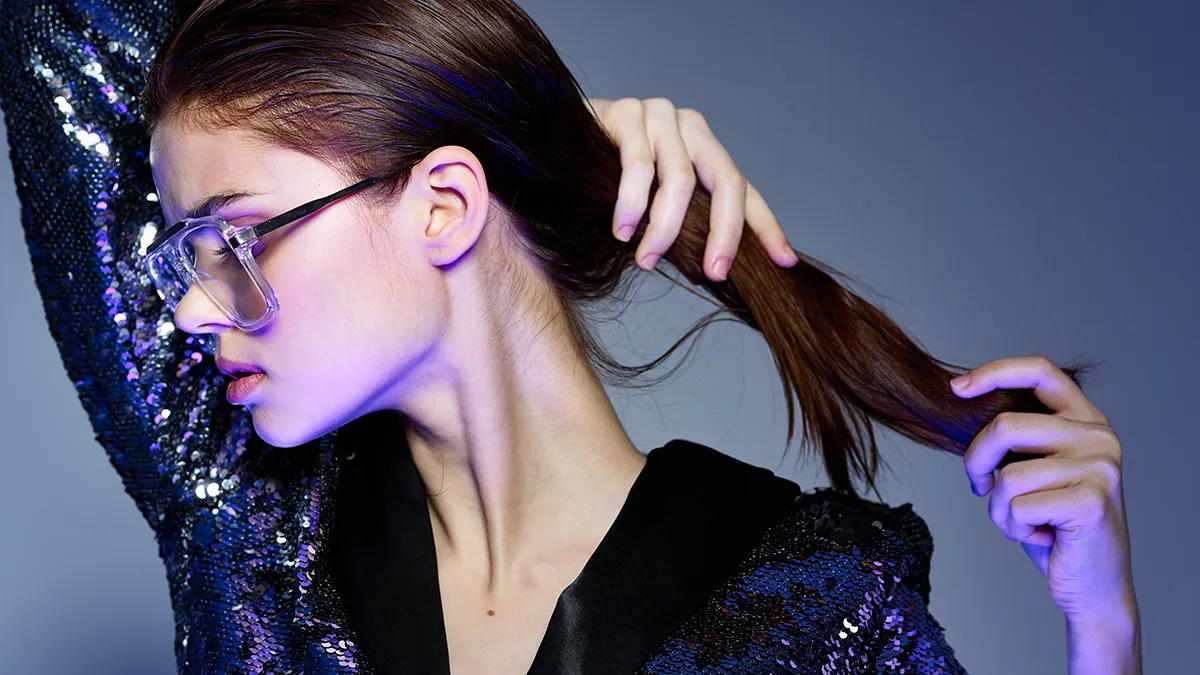 a woman in sequenced shirt applying coconut oil to hair