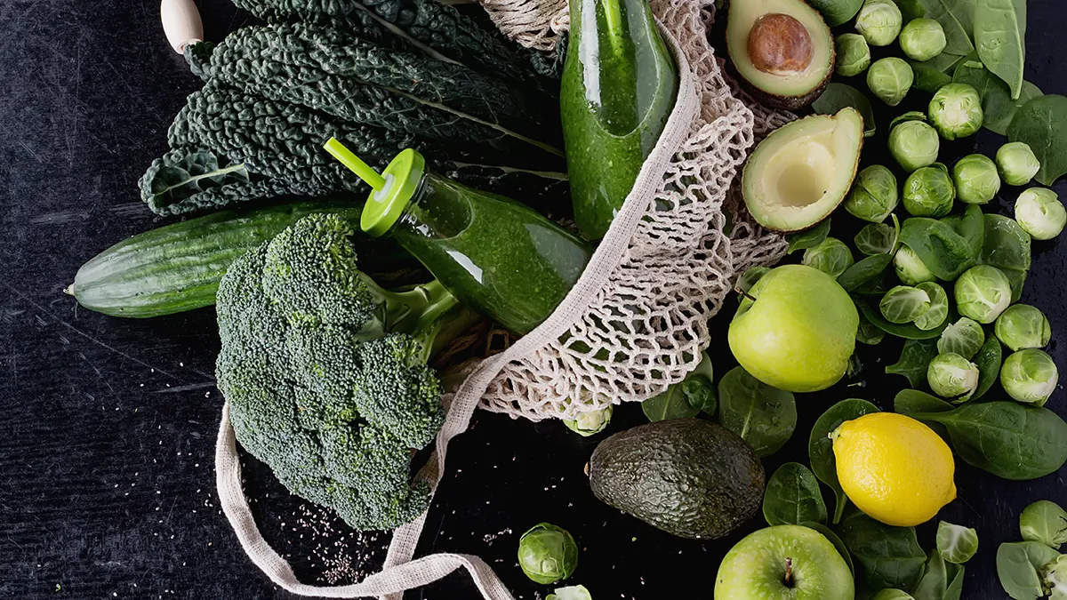 a lot of supergreens and citrus fruit in a white farmer's market grocery net on a dark table