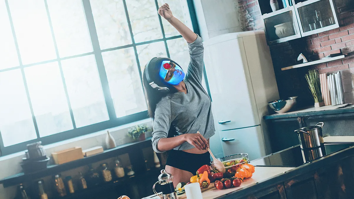 A woman dancing in a loose gray shirt and panties wearing FAQ 201 LED face mask while making lunch