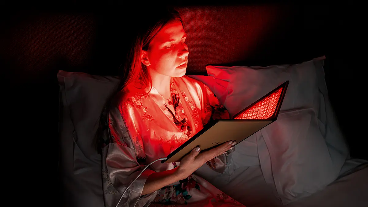 A woman using a red LED panel before sleep in bed