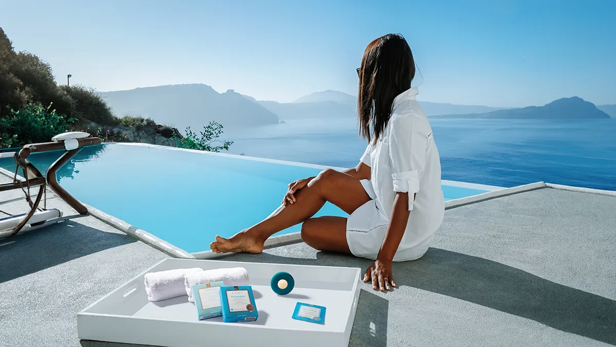 A woman in white by a beautiful pool with her FOREO UFO 3 go and UFO activated masks