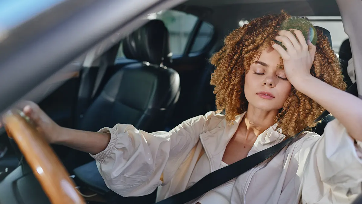 A tired woman dressed in light white clothing in a hot car
