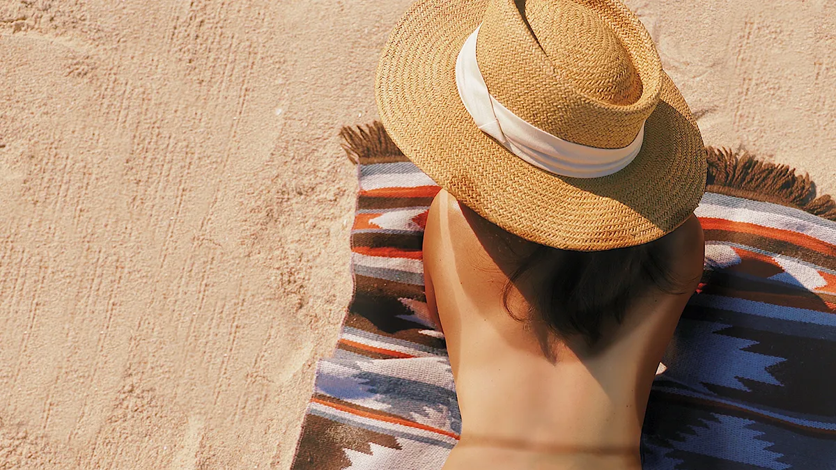 A topless woman with a very visible tan lines lying on her stomack on a sandy beach