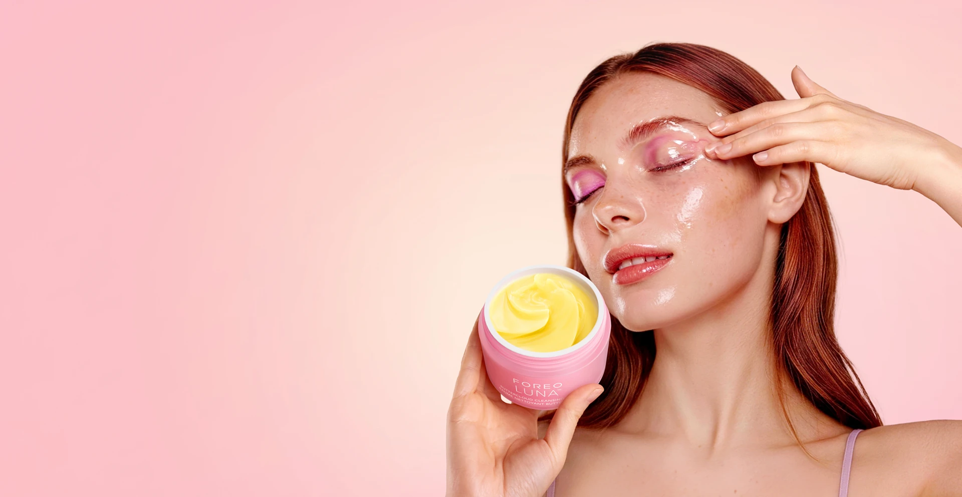Woman with closed eyes holding a pink jar of FOREO LUNA Buttercloud Cleansing Balm