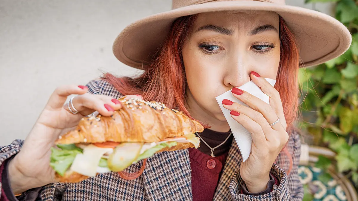 A woman feeling nauseous looking at a sandwich