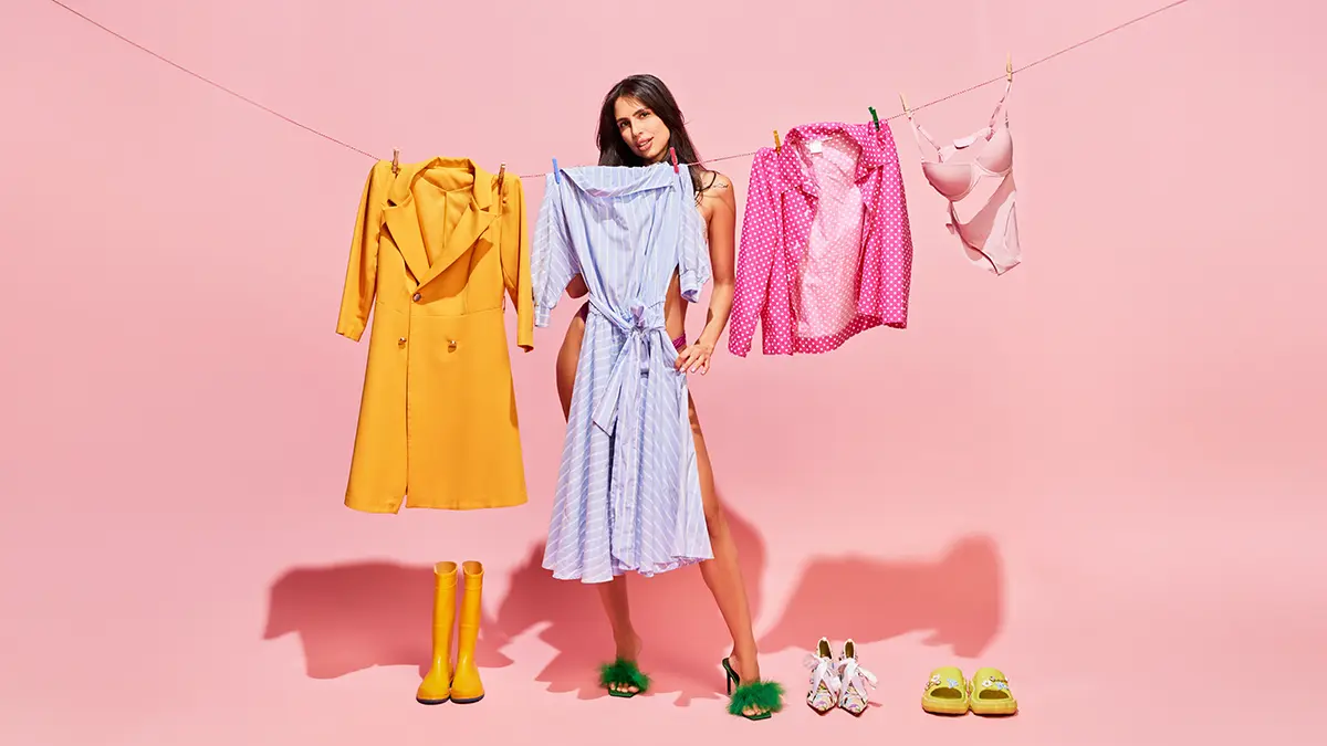A naked woman hiding behind a dress on a clothes line, on pink background