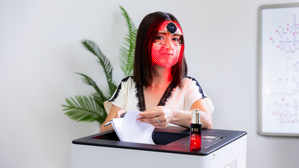 A woman using FAQ 202 silicone LED face mask in the office while working on a printer