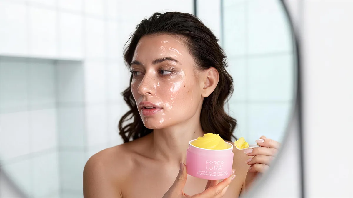 A woman using LUNA™ Buttercloud Cleansing Balm in front of the mirror