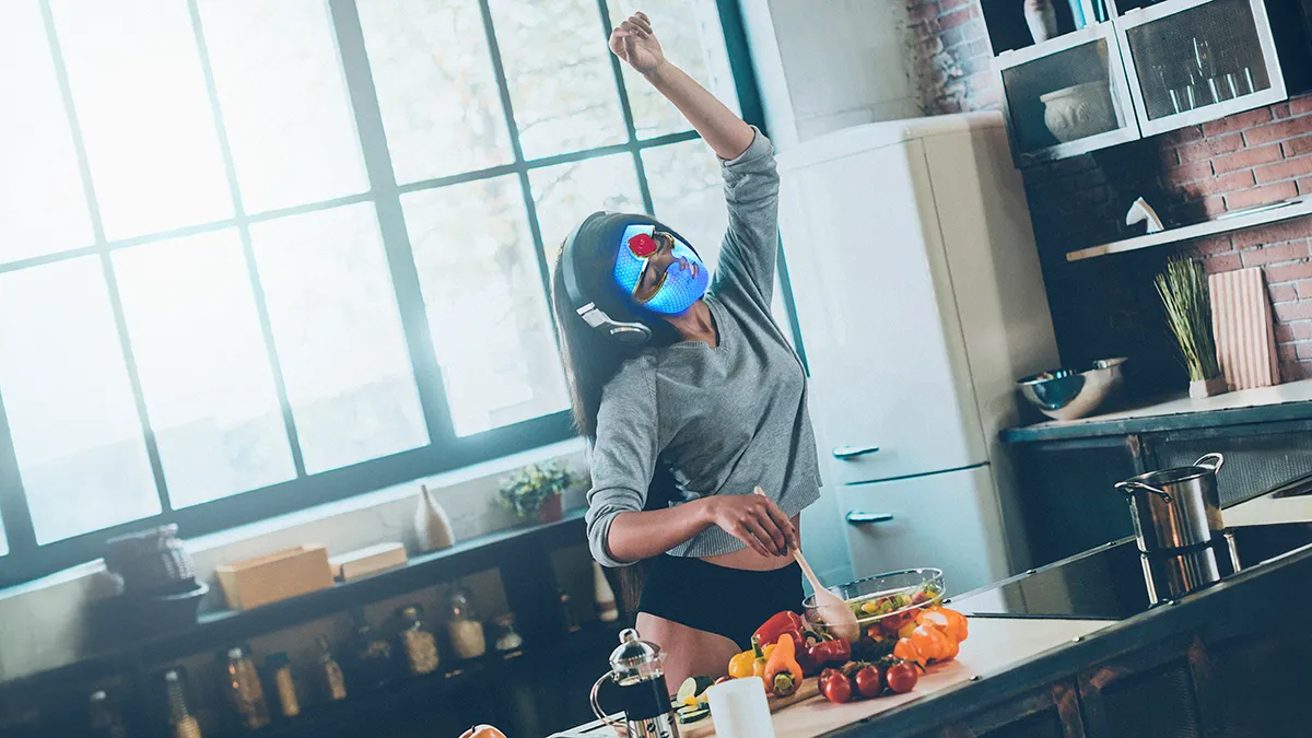 a woman cooking in her kitchen wearing an FAQ 201 blue light therapy mask for acne