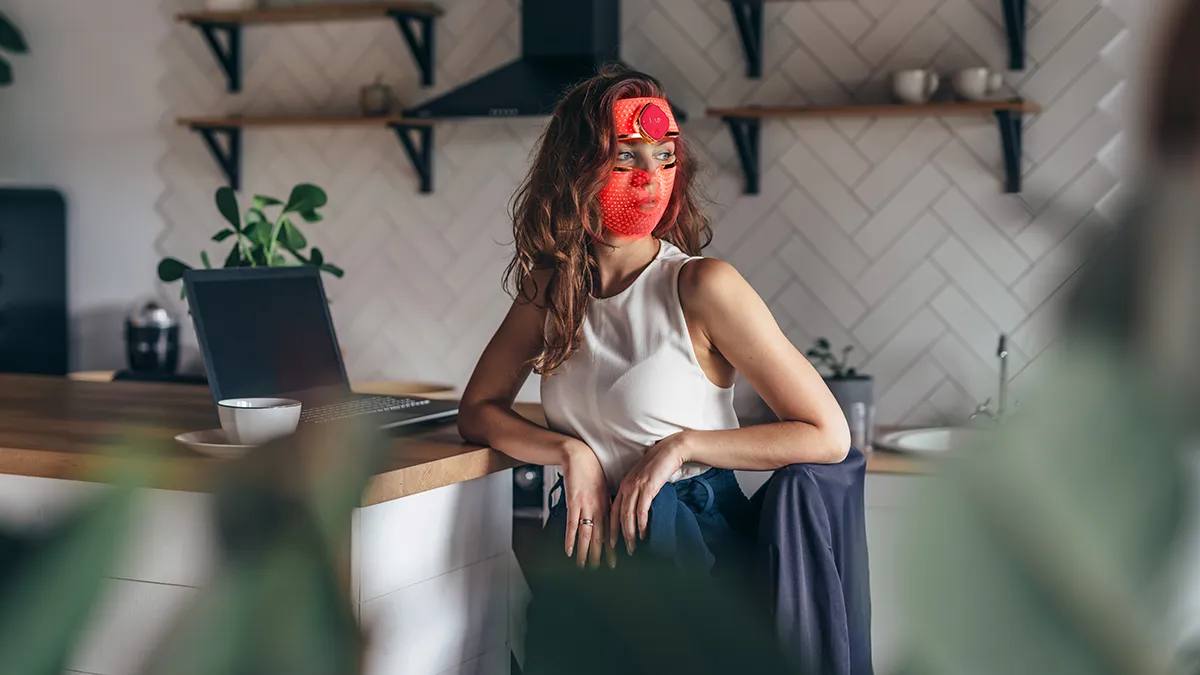 A woman wearing FAQ 201 in the office using red light for acne