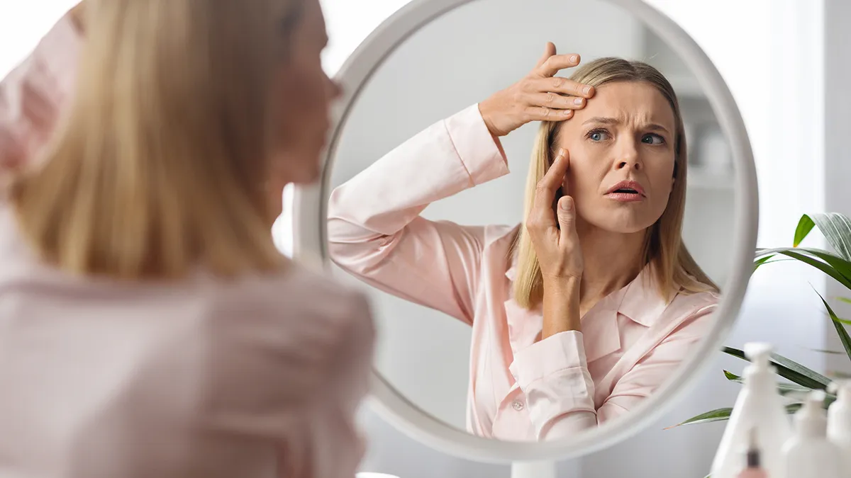 A woman in front of the mirror worrying about new wrinkles on her face