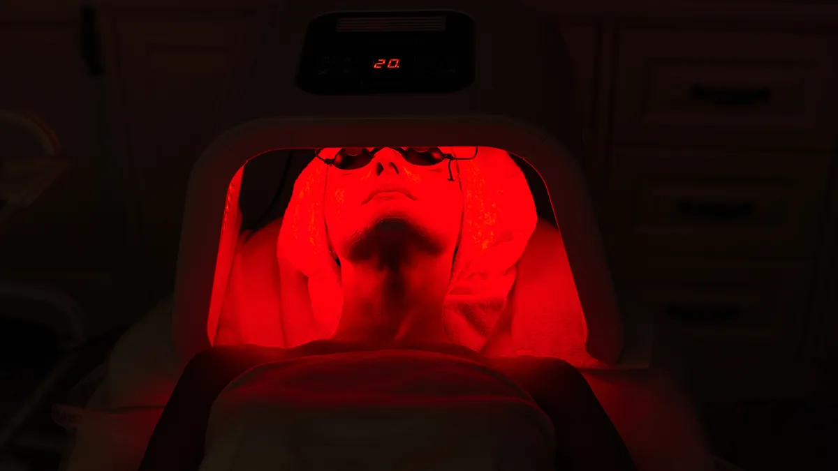 A woman lying in a machine using red light therapy for acne