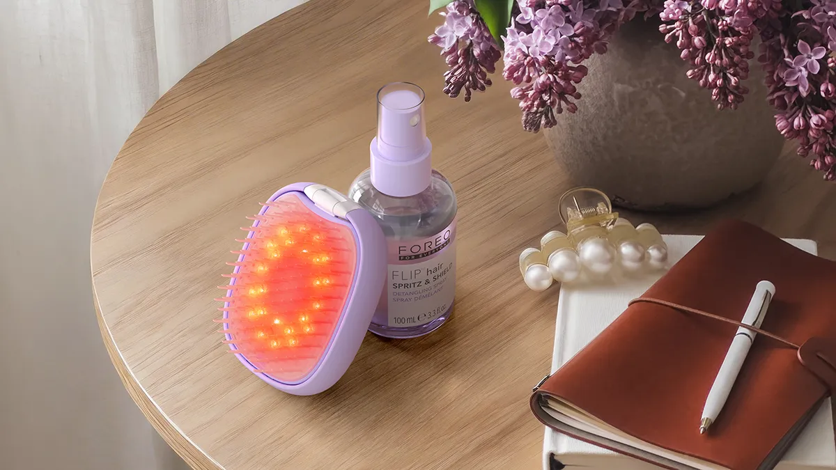 FLIP plus LED DETANGLING HAIRBRUSH and detangling spray on the table, next to a leather notebook and a hair clip