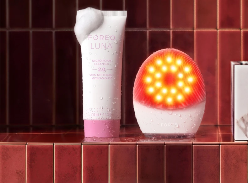 FOREO LUNA 5 LED with glowing lights beside a tube of LUNA cleanser on a tiled shelf