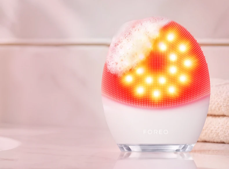 White FOREO LUNA 5 LED with glowing red lights and cleanser foam on its silicone touchpoints