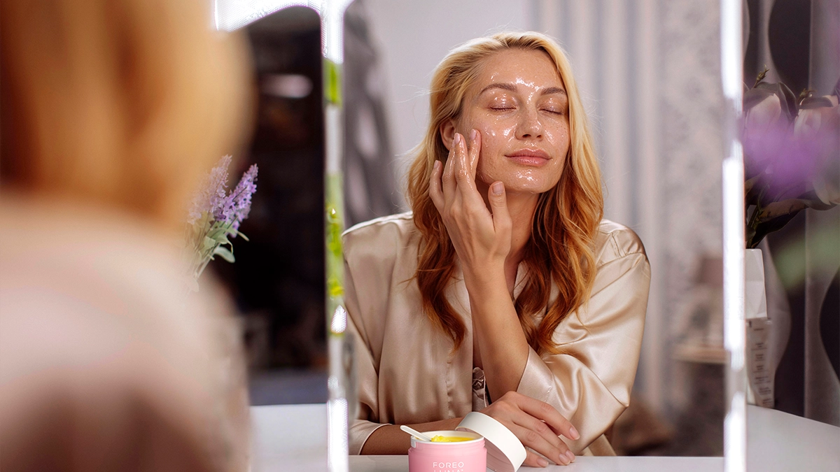 A woman using a balm to remove makeup in front of the mirror