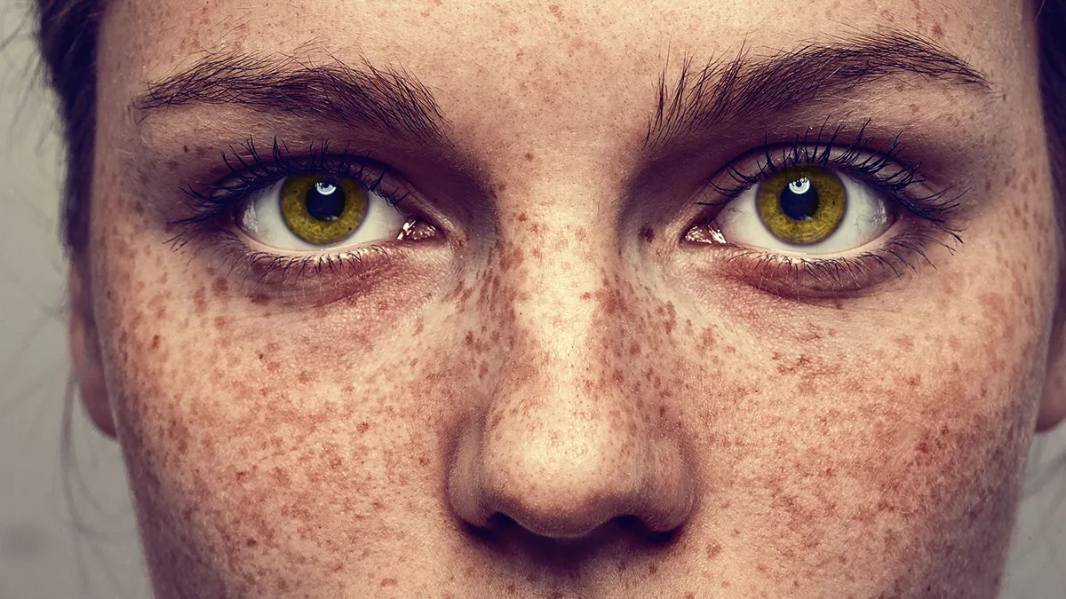 A closeup of a woman with beautiful eyes, fully eyebrows and gorgeous freckles