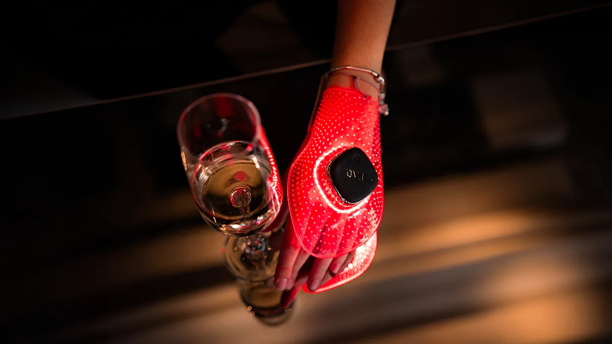 FAQ 221 red LED therapy for aging hands, a woman grabbin a champagne glass with a hand mask glowing red