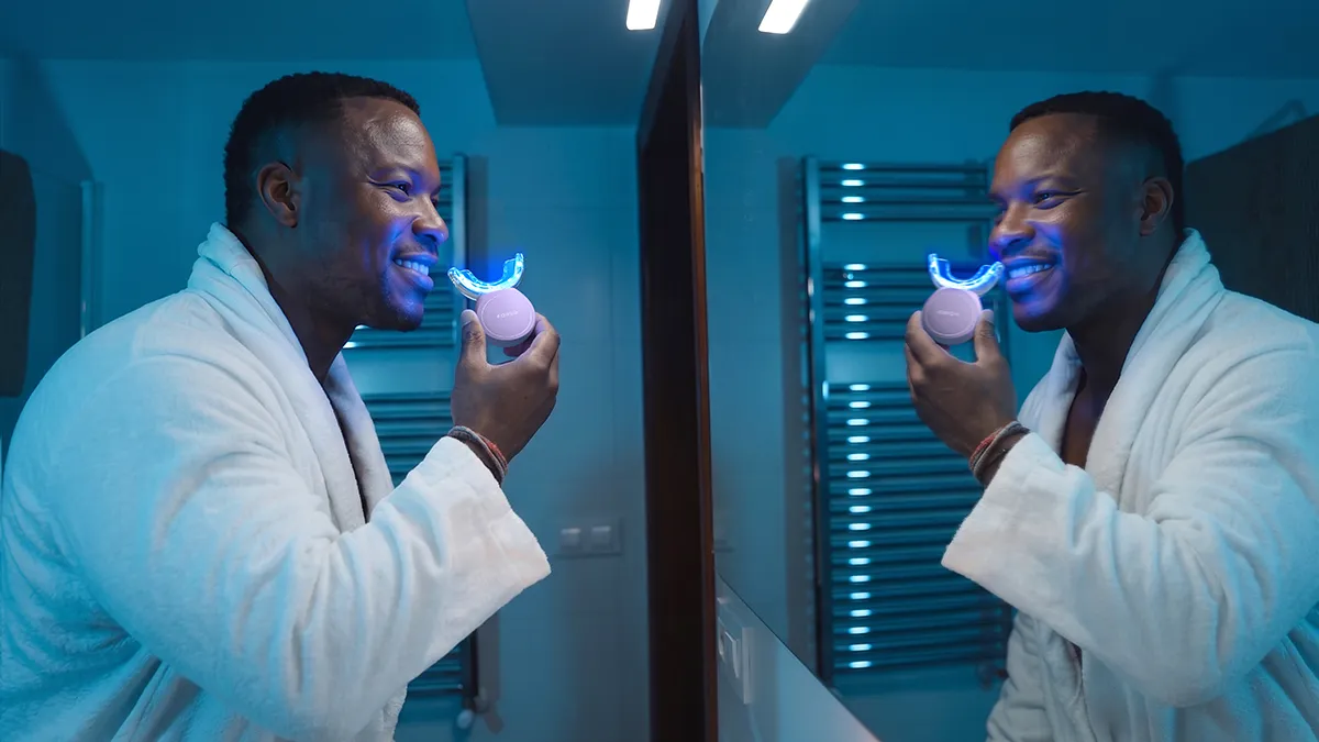 A man using issa teeth whitening device with blue LED in front of the mirror