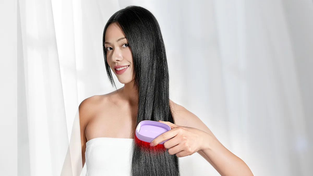 A woman with beautiful hair using hair loss LED hair brush in a white minimalist environment
