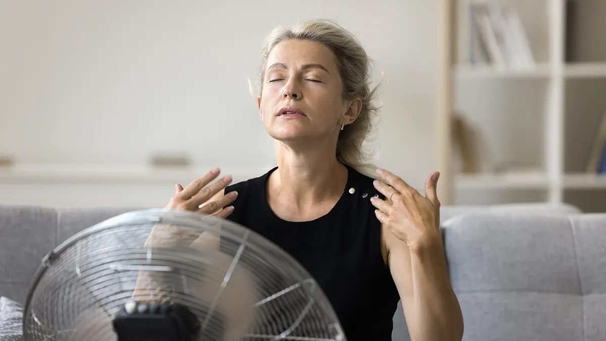 Woman sitting in front of a fan for manopause hot flashes
